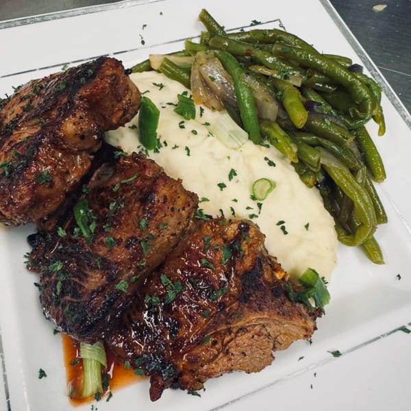 Two grilled lamb chops with mashed potatoes and green beans on a white plate.
