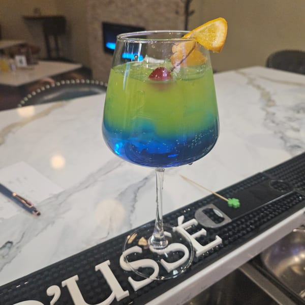 A vibrant blue and green cocktail with a cherry and orange slice, on a bar.
