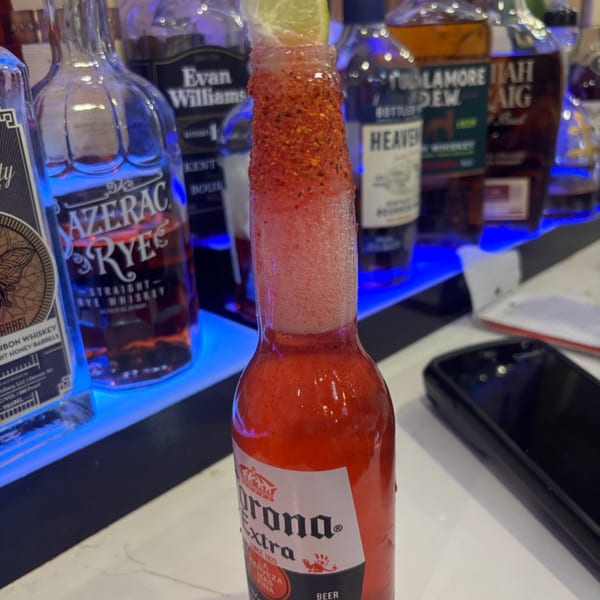 A Corona Extra beer bottle with red liquid, chili-lime rim, and a lime wedge at Harold's 25.
